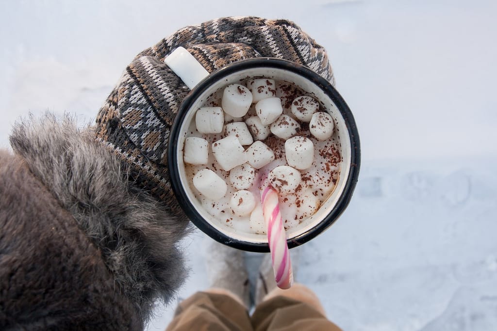 white and black mug with marshmallow and vegan hot cocoa amidst background of snow