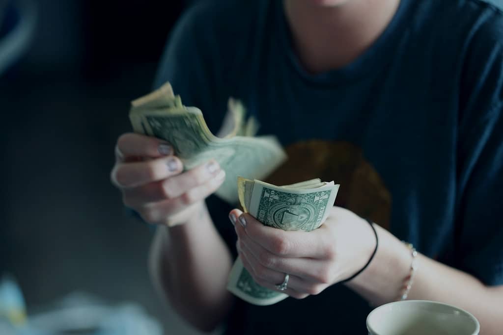focus photography of person counting dollar banknotes while indulging in consumerism