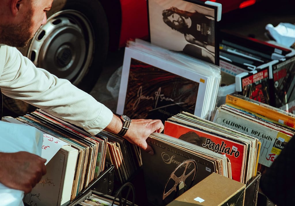 person holding vinyl records at a yard sale with clutter item for sale
