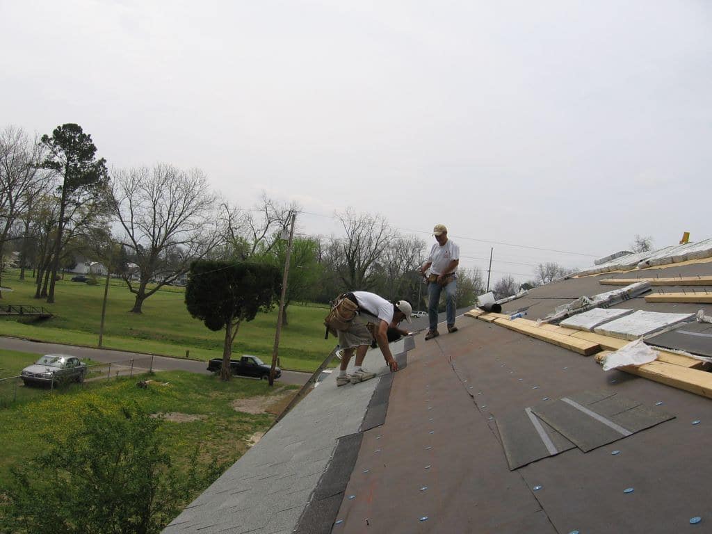 Putting asphalt shingles on a roof.