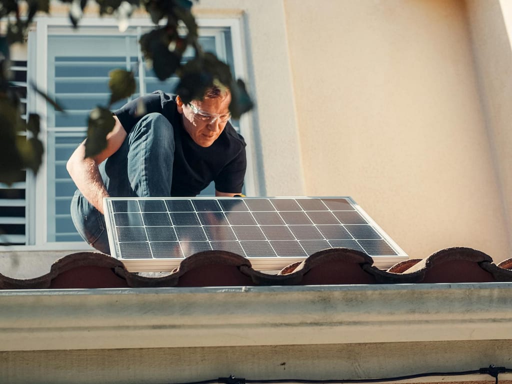 A Man in Black Shirt Installing a Green Home Improvement (Solar Panel) on the Roof