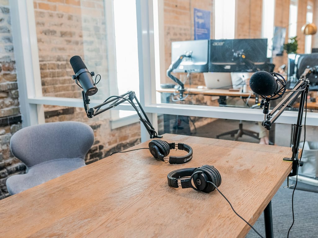 two black headphones on brown wooden table with a microphone stand, about to do a podcast introduction