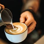 person preparing oat milk latte with art