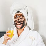 female having diy at home spa day with mud mask and mimosa in hand