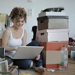 Smiling female on computer surrounded by clutter