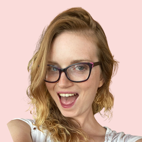 Ginny Rayne headshot. Glasses, big smile, pink background