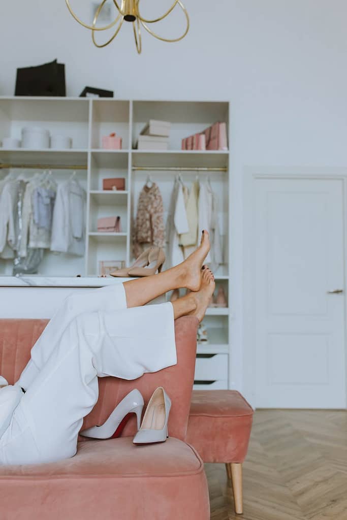 Woman in White Pants Lying on Pink Sofa in cluttered closet with Barefoot Up