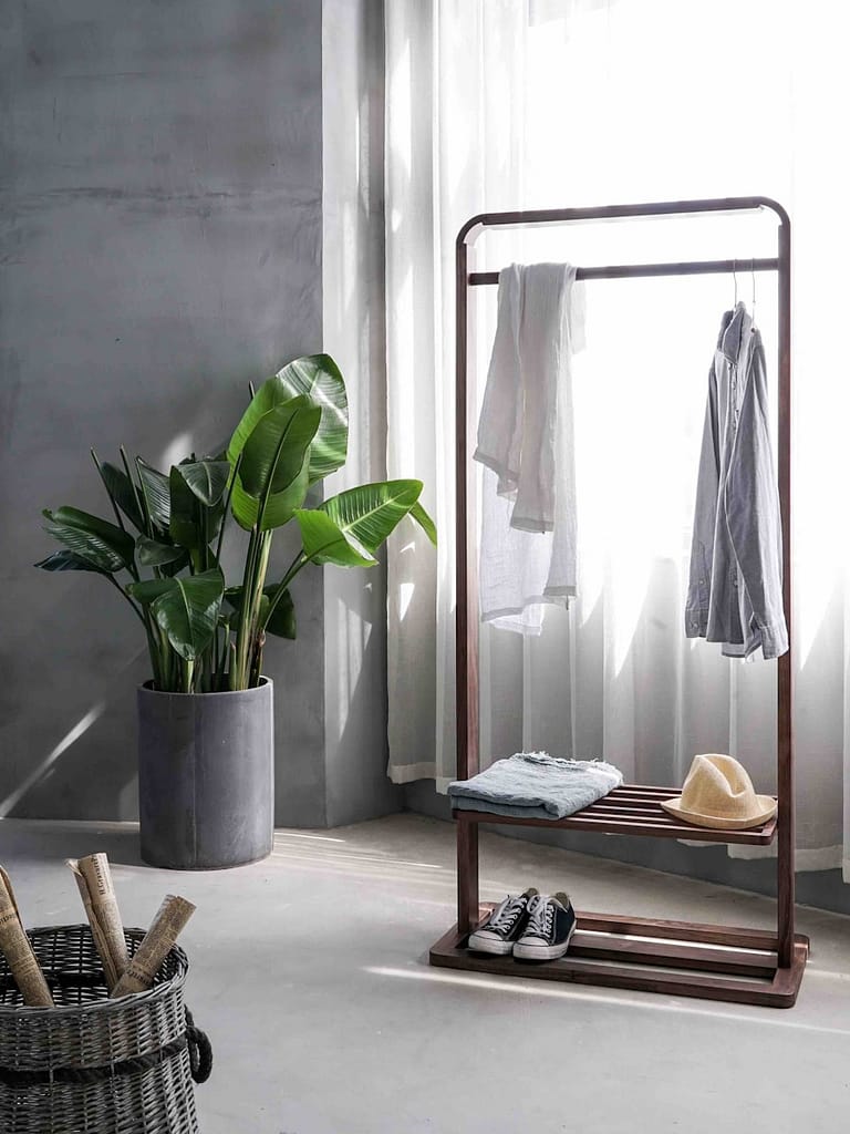 gray dress shirt hang on brown wooden rack in front of window with white curtain in an organized, minimalist space