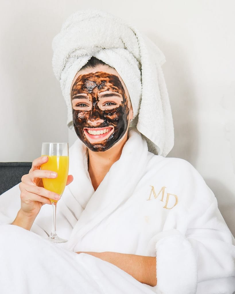 female having diy at home spa day with mud mask and mimosa in hand